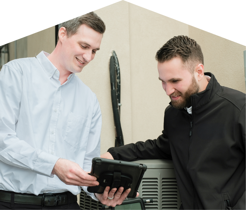 A Peel technician in a white shirt shows service details on a tablet to a smiling client in a black jacket, standing beside an AC unit outside a beige building.