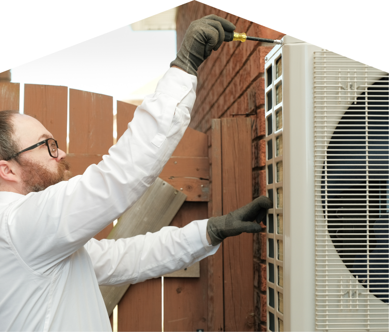 Peel service personnel working on an AC condenser, using a screwdriver to secure the unit's panel outdoors beside a wooden fence.