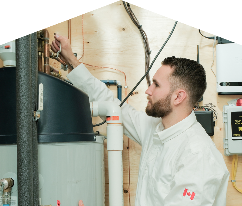 Peel water heater specialist adjusts piping on a large residential unit during a repair service, with exposed wood paneling and mounted utility components in the background.